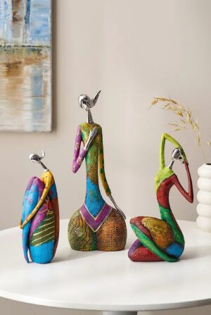 Figurka abstrakcyjna kobieta z żywicy, kolorowa, 23-35 cm, 3 modele - okrągły biały stolik kawowy w jasnym salonie, trzy figurki obok tacy i książki bez napisów