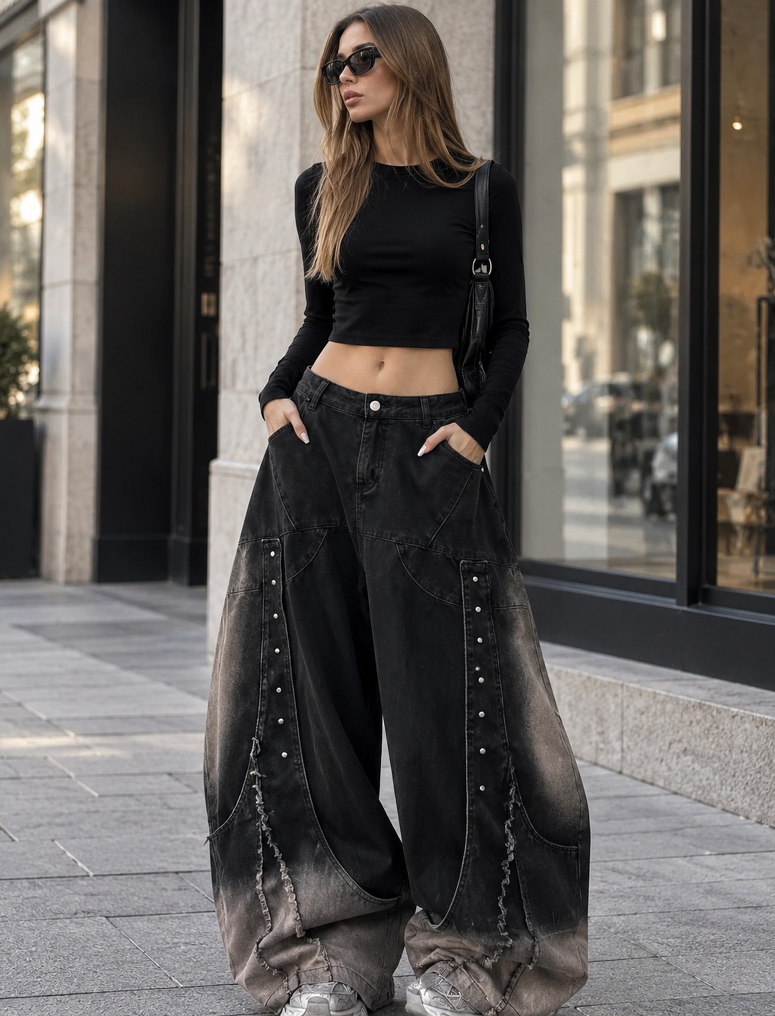 modelka w czarnych jeansach baggy i krótkim czarnym topie na miejskiej ulicy, dłonie w kieszeniach