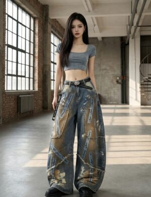 Jeansy damskie baryłkowe patchwork z postrzępionymi łatami, wysoki stan - sesja w industrialnej hali z betonową posadzką, krótki szary top, czarne masywne buty