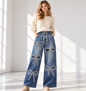 Jeansy damskie szerokie z kokardami z cyrkonii, gumka w pasie, L-4XL - modelka w jasnym kremowym swetrze, jasne studio, spodnie w całości widoczne