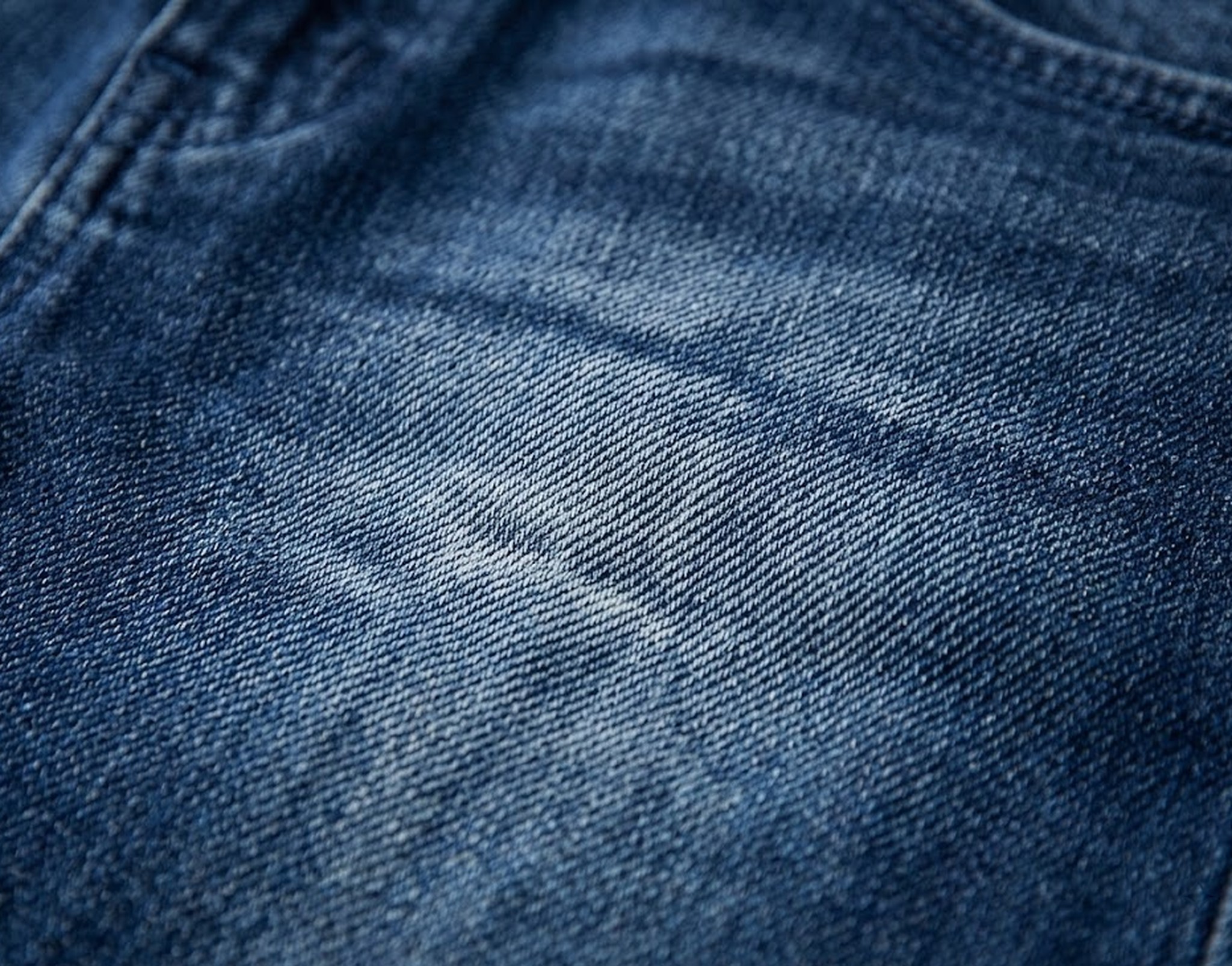 zbliżenie faktury ciemnego, spranego denimu z rozjaśnieniem na udzie