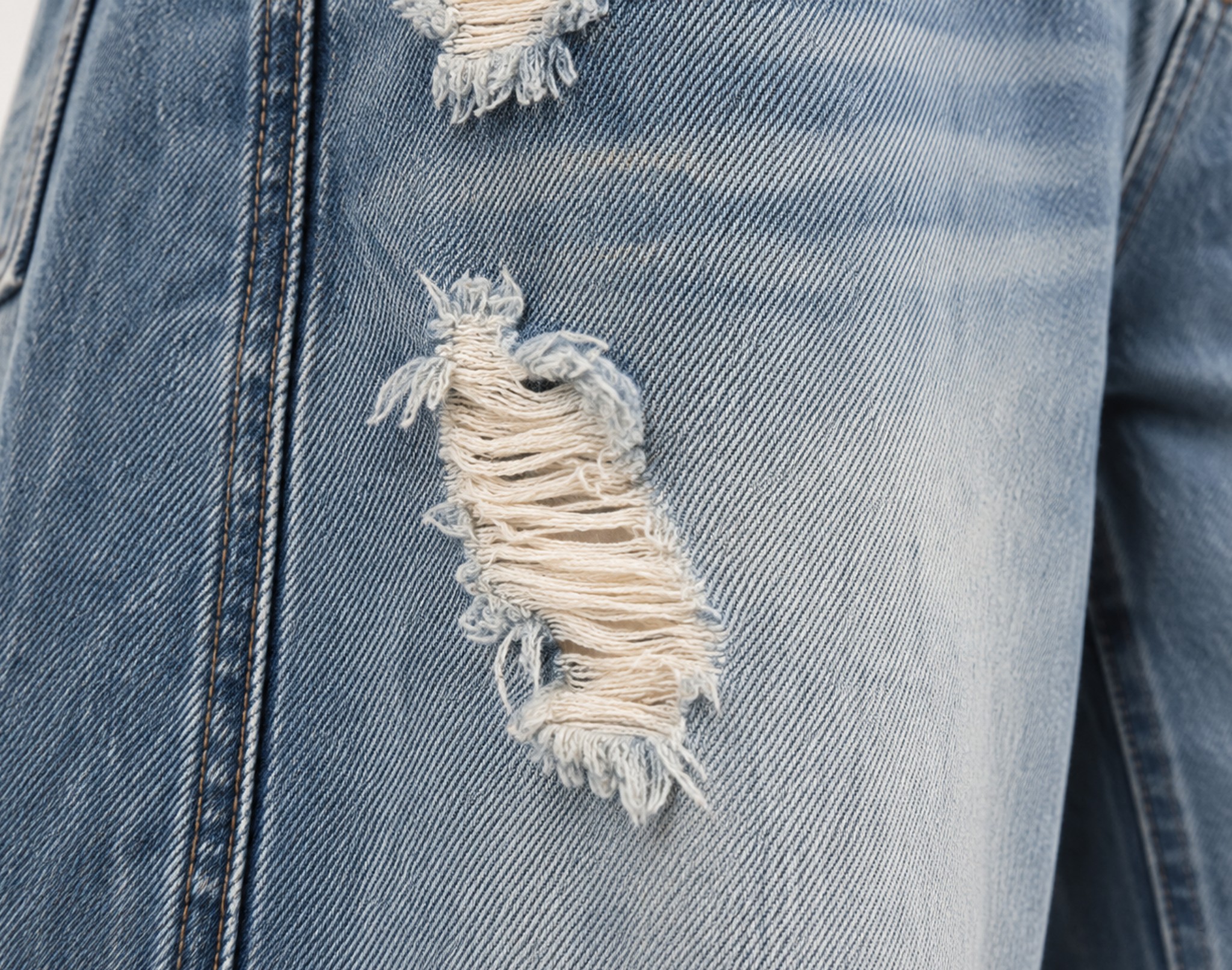 zbliżenie przetarć z postrzępionymi nitkami na udzie, jasny sprany denim