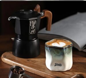 Kubek ceramiczny Bincoo 180 ml bez ucha, nieregularny kształt, do kawy - drewniany stół kuchenny z kawiarką i książką, poranne światło