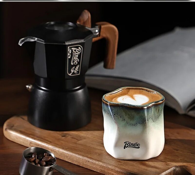 Kubek ceramiczny Bincoo 180 ml bez ucha, nieregularny kształt, do kawy - drewniany stół kuchenny z kawiarką i książką, poranne światło