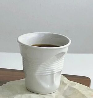 Kubek ceramiczny zgnieciony 200 ml, biały, do kawy i espresso - gładki kubek z kawą na stole