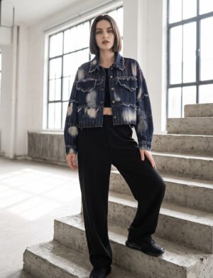 Kurtka jeansowa damska krótka patchwork z przetarciami, granatowa - betonowe schody w industrialnym wnętrzu, modelka w kurtce zapiętej, czarne sneakersy