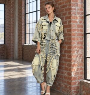 Damska kurtka lub spodnie haremki z frędzlami i dziurami, vintage - industrialne studio z ceglaną ścianą, modelka w niebieskim komplecie, bez napisu marki