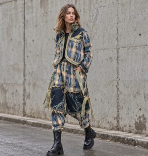 Kurtka i spodnie haremki damskie patchwork w kratę, efekt denimu - modelka w pełnym komplecie na miejskiej ulicy z betonową ścianą, botki na grubej podeszwie