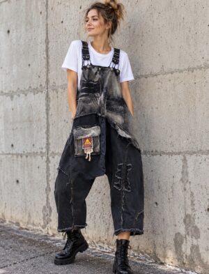 Ogrodniczki jeansowe damskie patchwork, luźne z obniżonym krokiem - modelka w ogrodniczkach i białym T-shircie przy betonowej ścianie