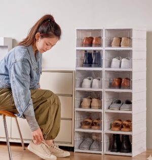 Organizer na buty 6 poziomów z przezroczystymi drzwiczkami, składany - kobieta zakłada buty obok kolumny w przedpokoju, buty bez logo