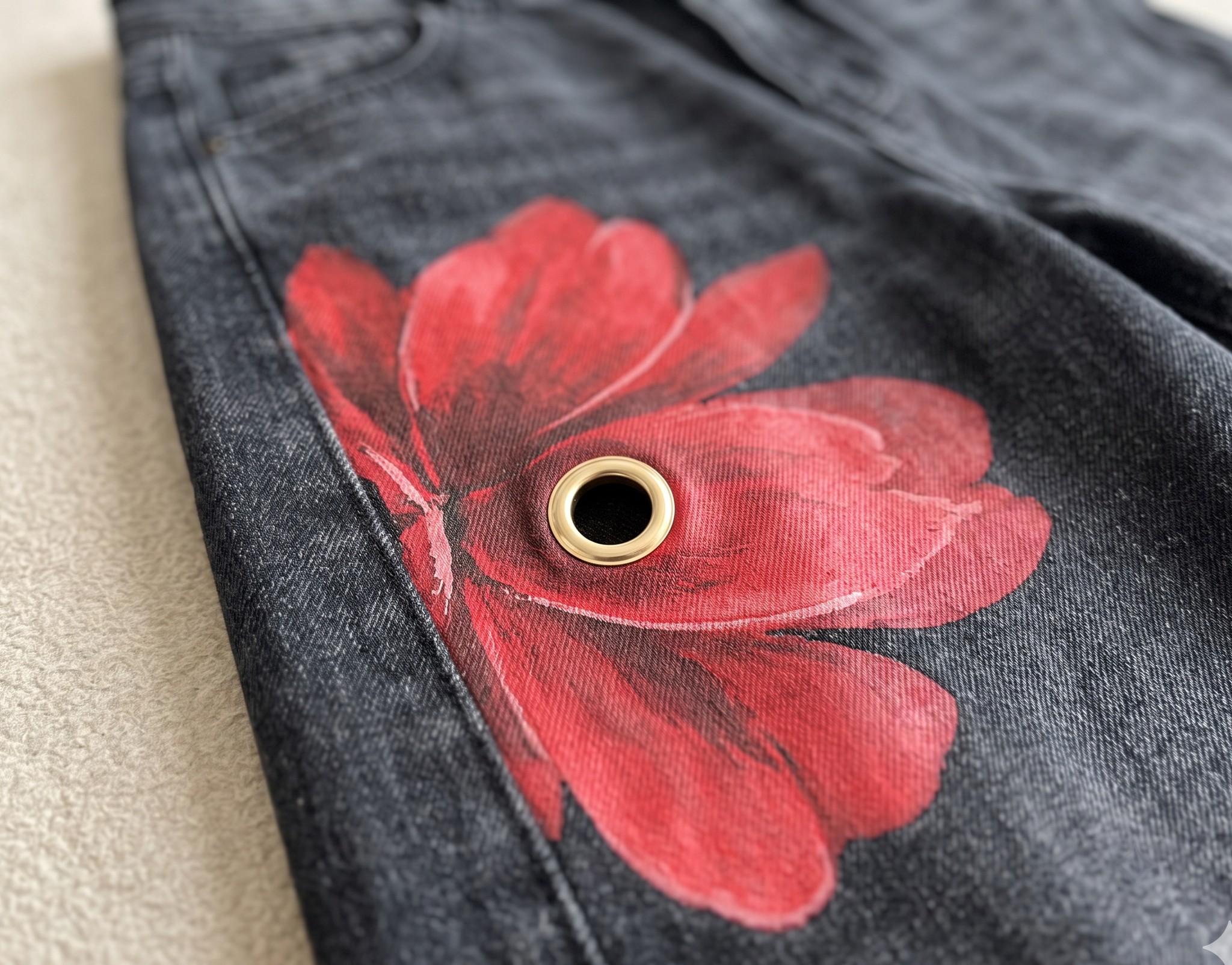 zbliżenie nadruku dużego czerwonego kwiatu na czarnej tkaninie imitującej sprany jeans