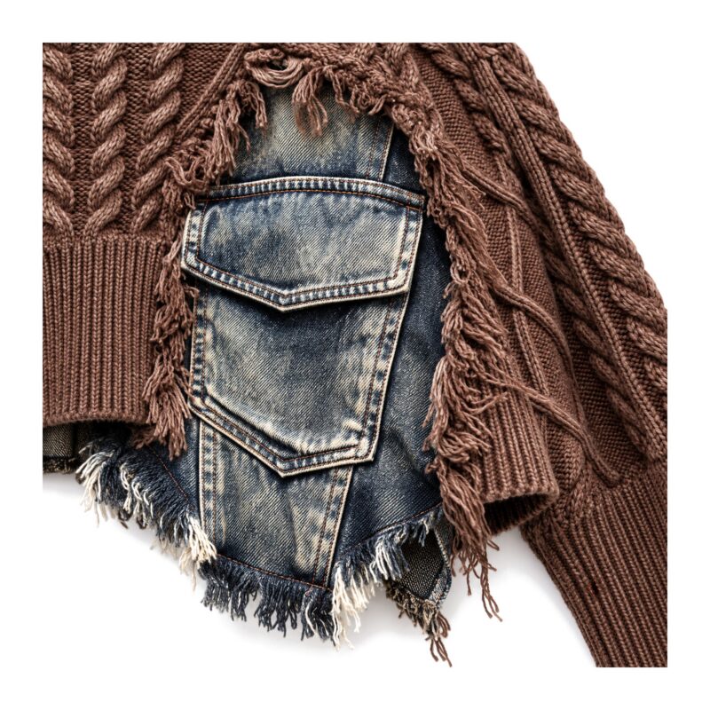 Sweter damski oversize z warkoczami i wstawkami z denimu, postrzępiony - zbliżenie wstawki z denimu z klapką i postrzępionego brzegu na brązowym swetrze, białe tło