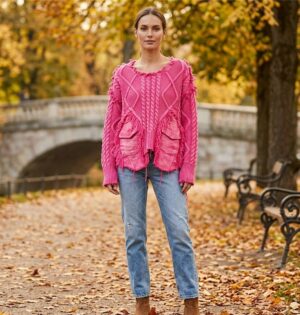 Sweter damski oversize z warkoczami i jeansowymi kieszeniami, patchwork - jesienna sesja w parku: modelka w swetrze fuksja z jasnymi jeansami i botkami